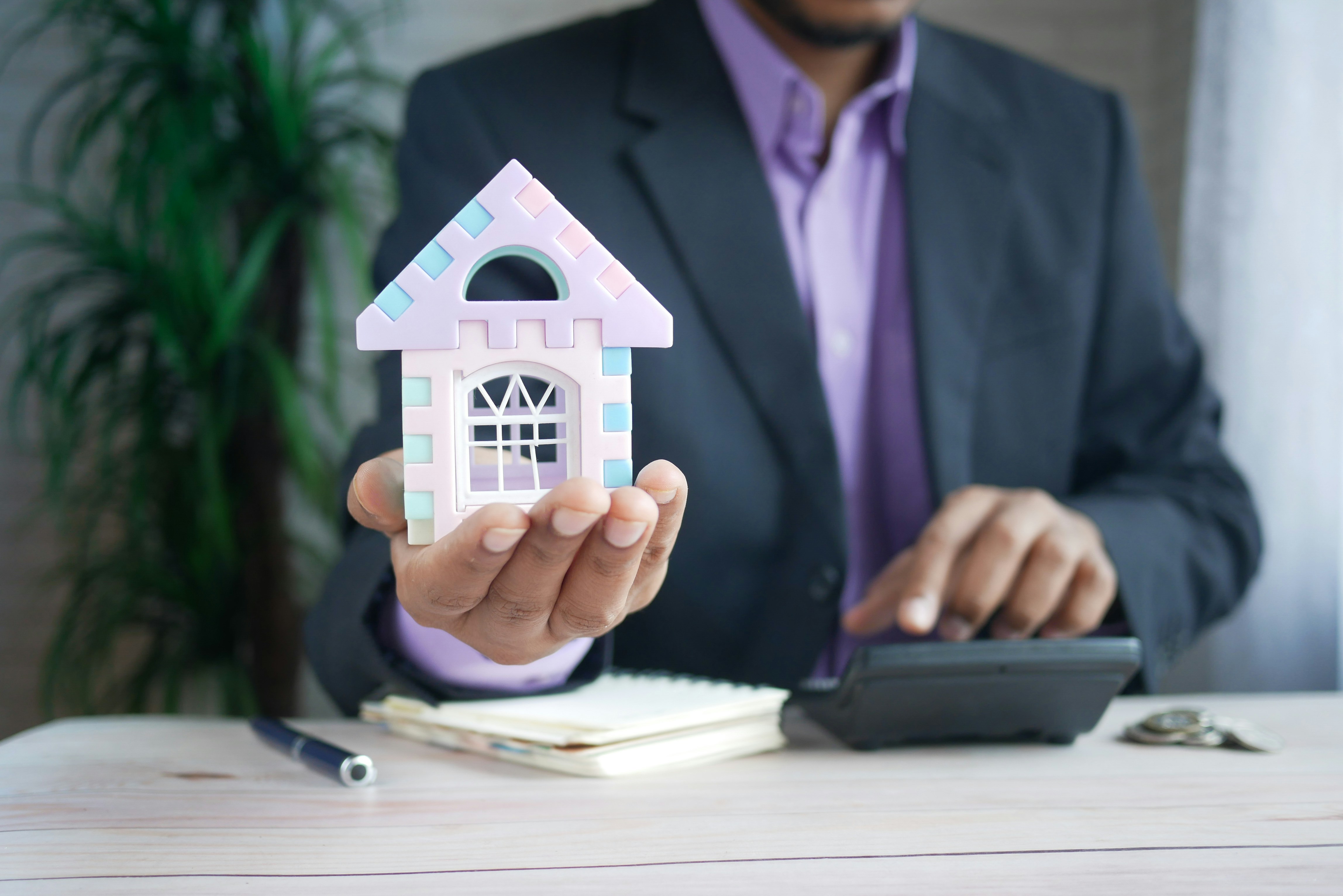 sistem-kasir-investasi-dan-hitung-keuangan-properti-kasair Agen atau pebisnis properti memegang miniatur rumah dan menggunakan kalkulator untuk menghitung keuangan dengan Kasair POS