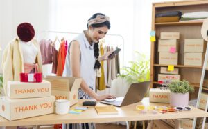 Pemilik bisnis ritel online shop busana menggunakan laptop dan HP untuk kelola stok dan pesanan paket dengan Kasair POS