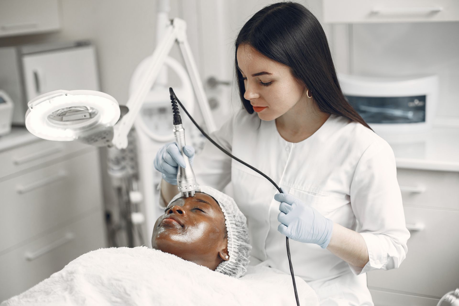 Layanan Perawatan Wajah Klinik Kecantikan Terapis kecantikan sedang melakukan perawatan wajah pasien menggunakan alat facial modern di klinik kecantikan