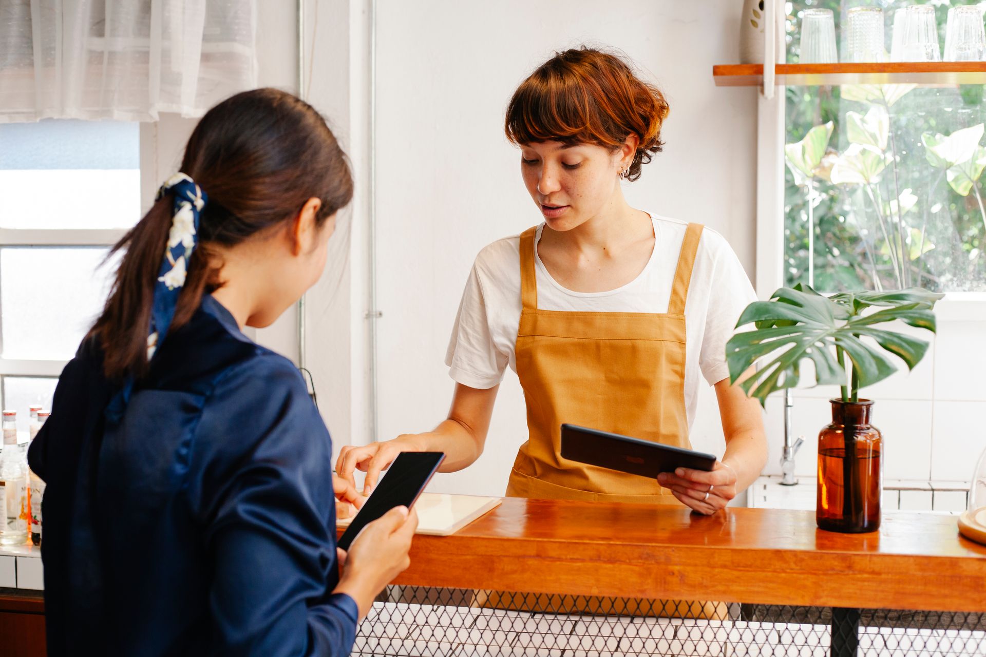 Transaksi Cashless Kasir Kafe Modern Kasir kafe berapron melayani pembayaran non-tunai pelanggan menggunakan tablet kasir POS di meja counter