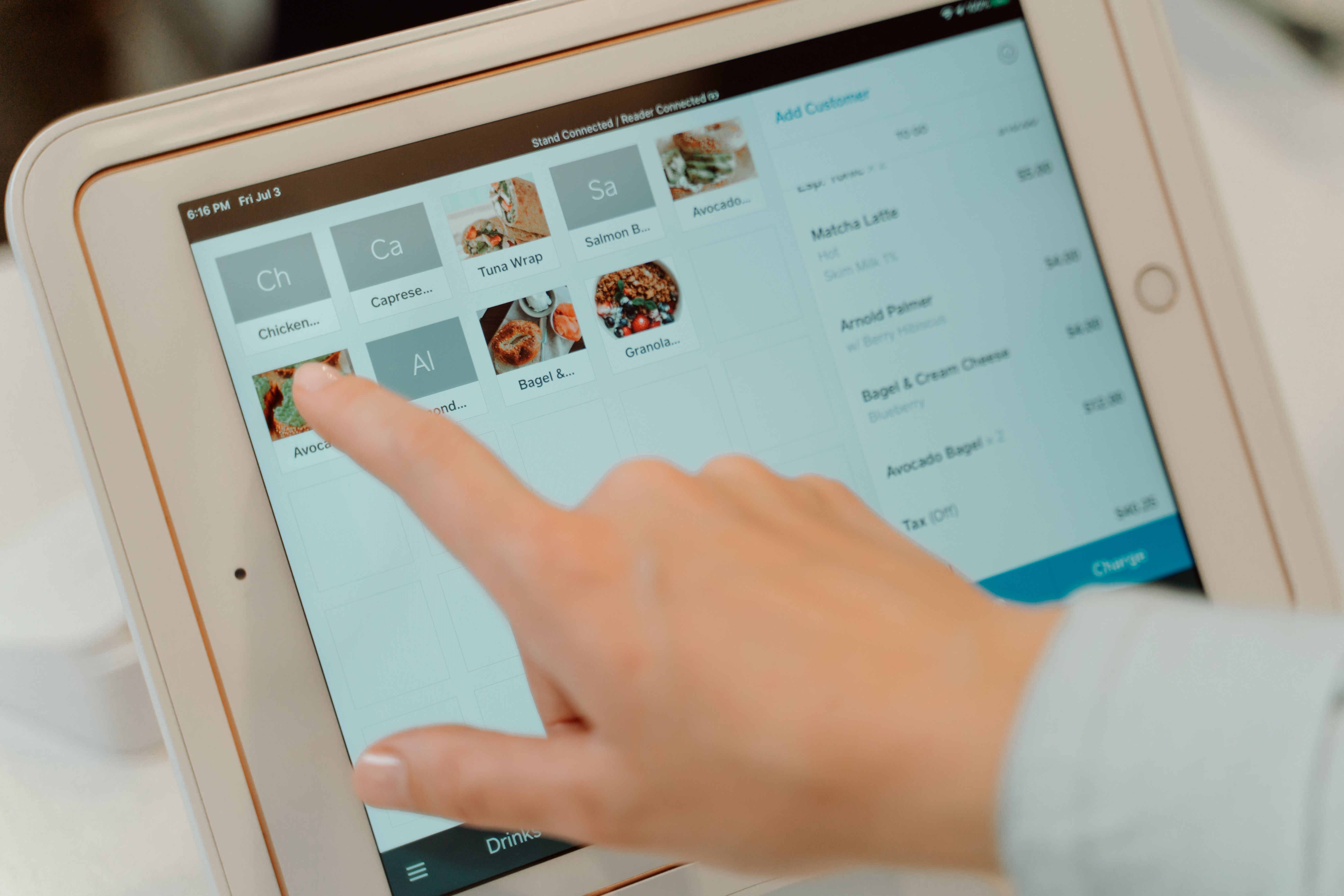 Jari tangan kasir sedang memilih menu pesanan makanan pada tablet aplikasi kasir POS.