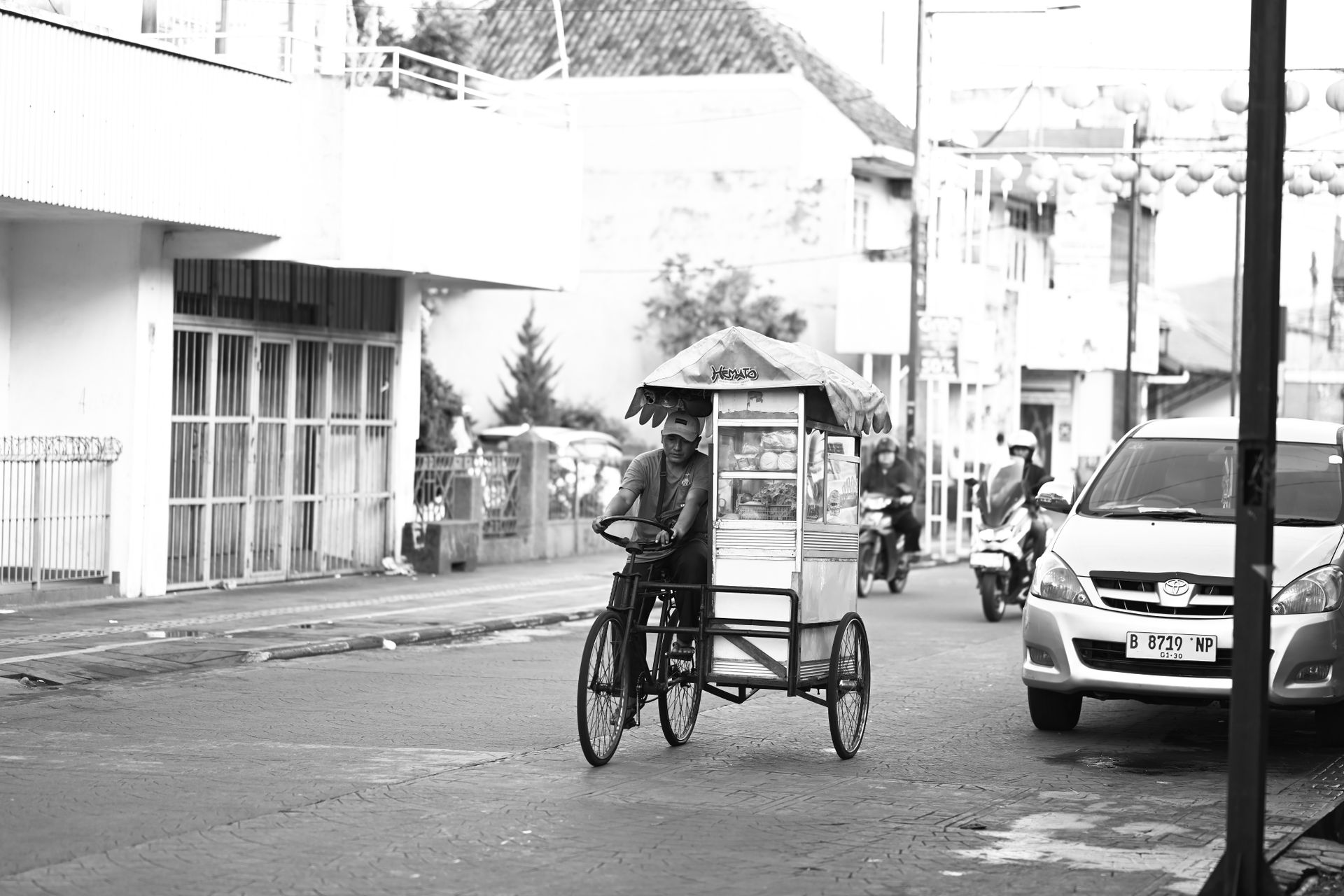 Pedagang makanan keliling mengendarai becak gerobak usaha di jalanan perkotaan bernuansa hitam putih