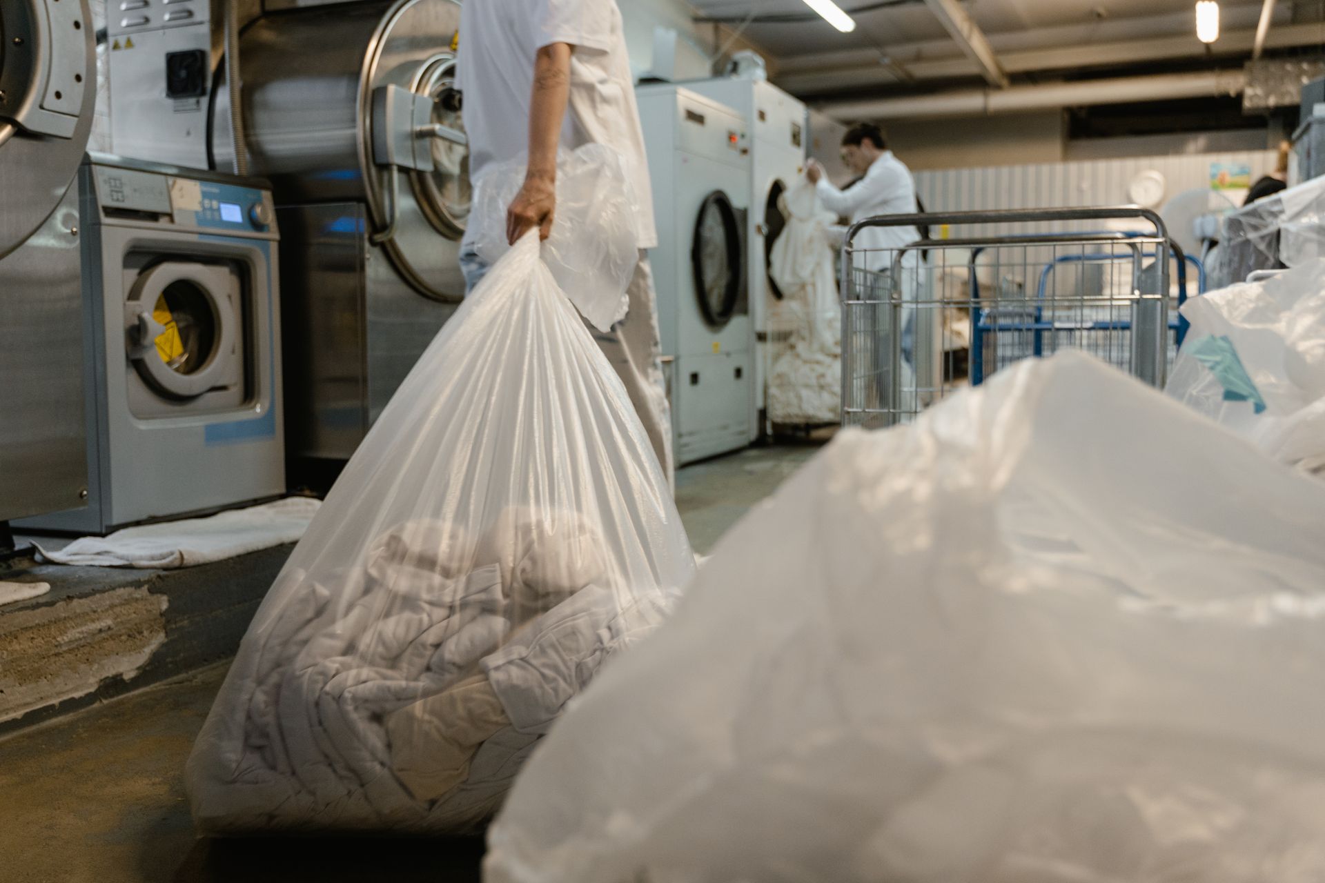 Pekerja laundry industri membawa kantong cucian di area mesin cuci komersial