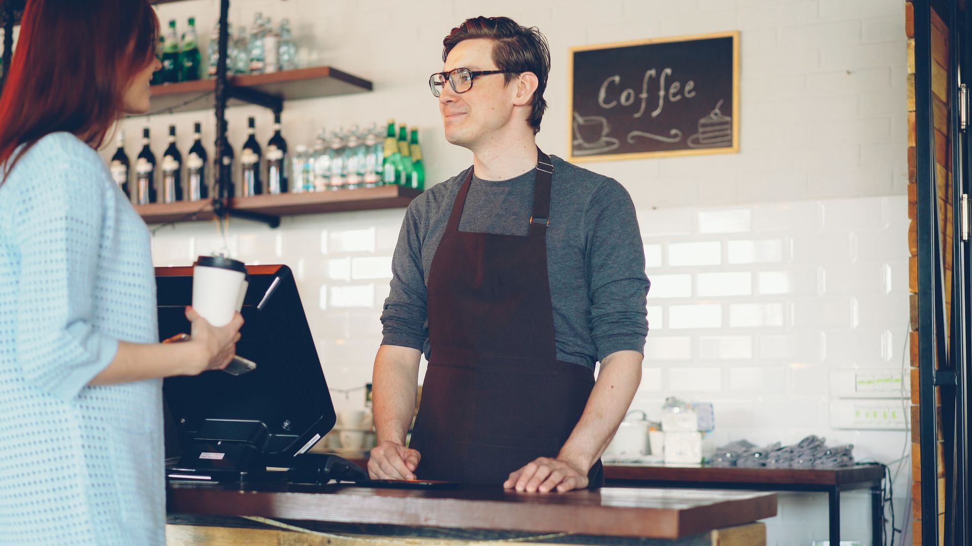 pelayanan-pelanggan-dengan-sistem-kasir-digital Barista melayani pelanggan di meja kasir sebuah kedai kopi
