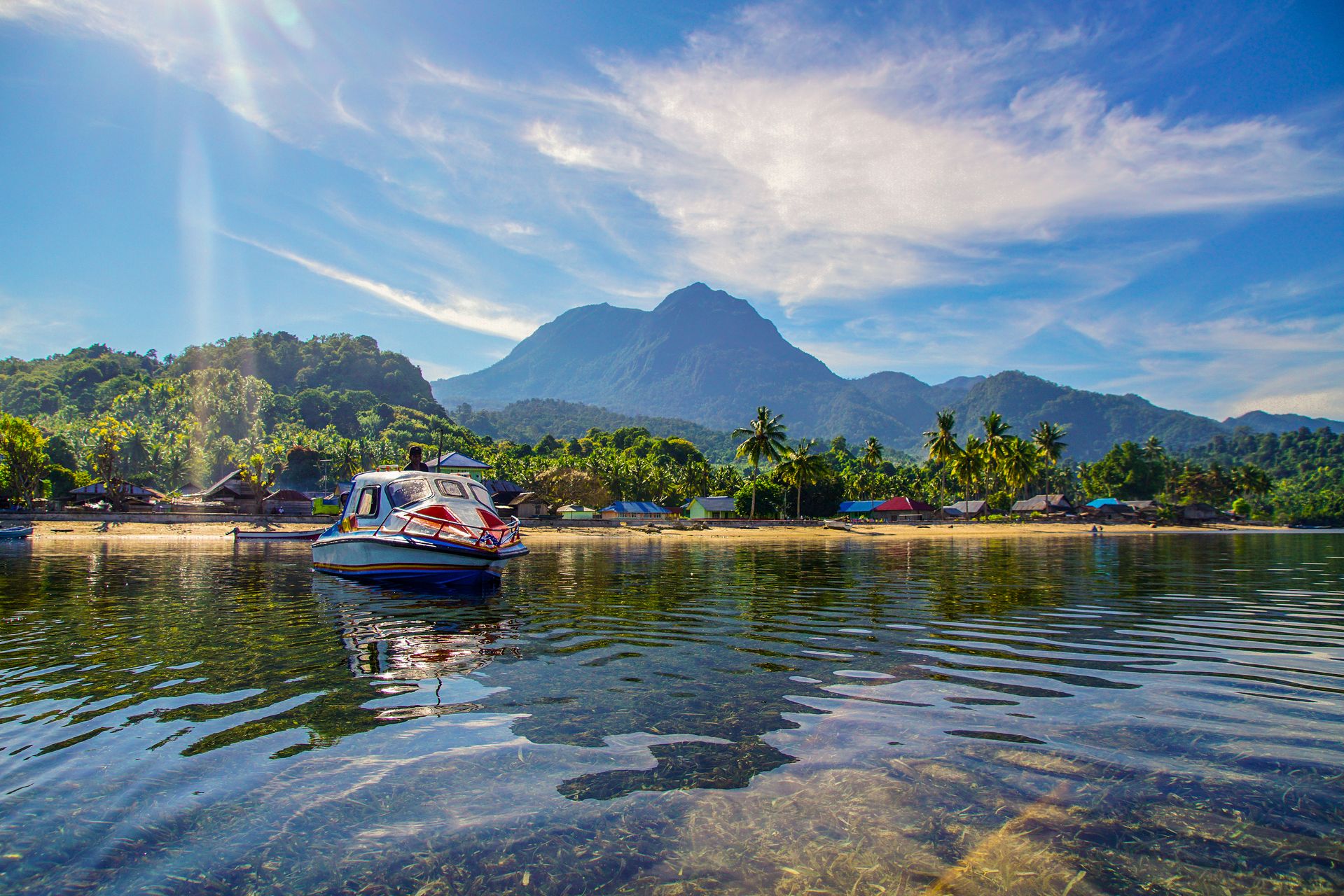 Pemandangan perairan tenang dengan perahu dan pegunungan hijau di kawasan wisata