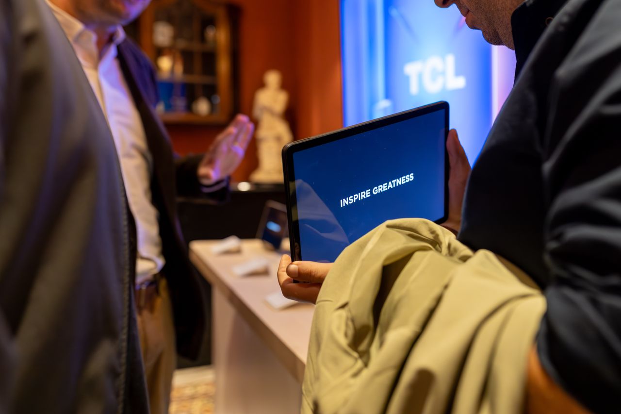 Seseorang memegang tablet PC dengan tampilan layar bertuliskan INSPIRE GREATNESS dalam acara pameran teknologi TCL.