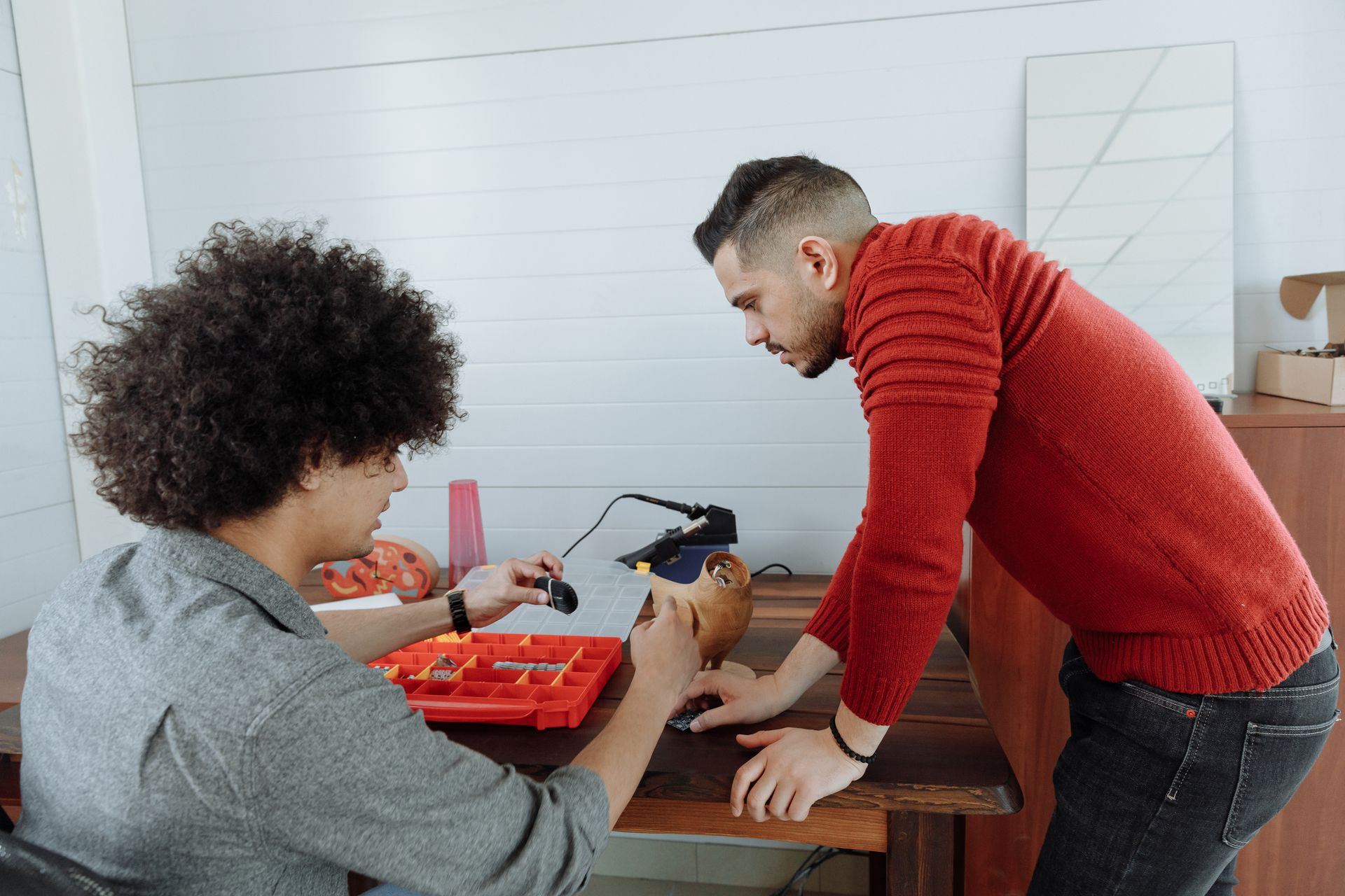 Kolaborasi-Pekerja-Merakit-atau-Memperbaiki-Komponen-Elektronik Dua pria berdiskusi dan merakit komponen kecil di meja kerja bengkel atau studio