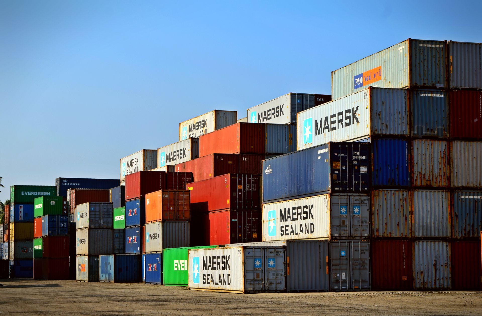 sistem-kasir-dan-manajemen-rantai-pasok-logistik-kasair Tumpukan kontainer kargo di depo logistik untuk manajemen rantai pasok dan distribusi barang terintegrasi Kasair POS