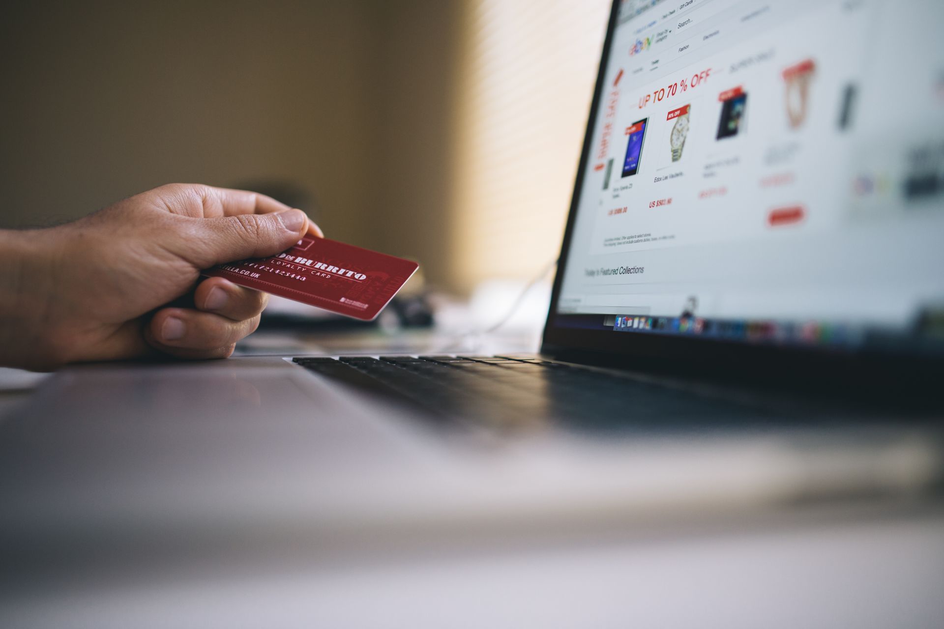 Seseorang memegang kartu kredit di depan laptop saat berbelanja online di situs e-commerce