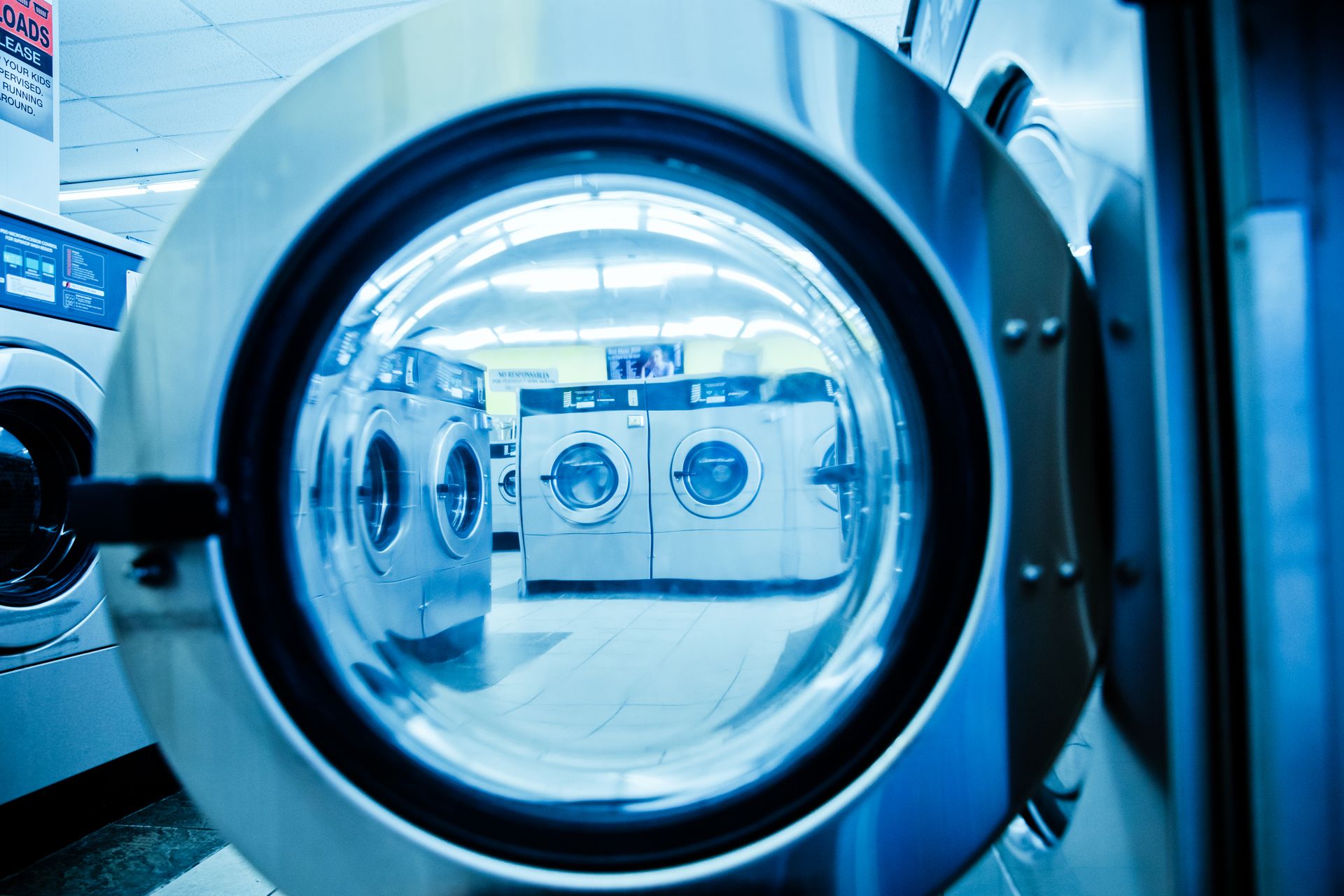 Tampilan dalam pintu kaca mesin cuci di laundromat dengan deretan mesin cuci berlampu biru