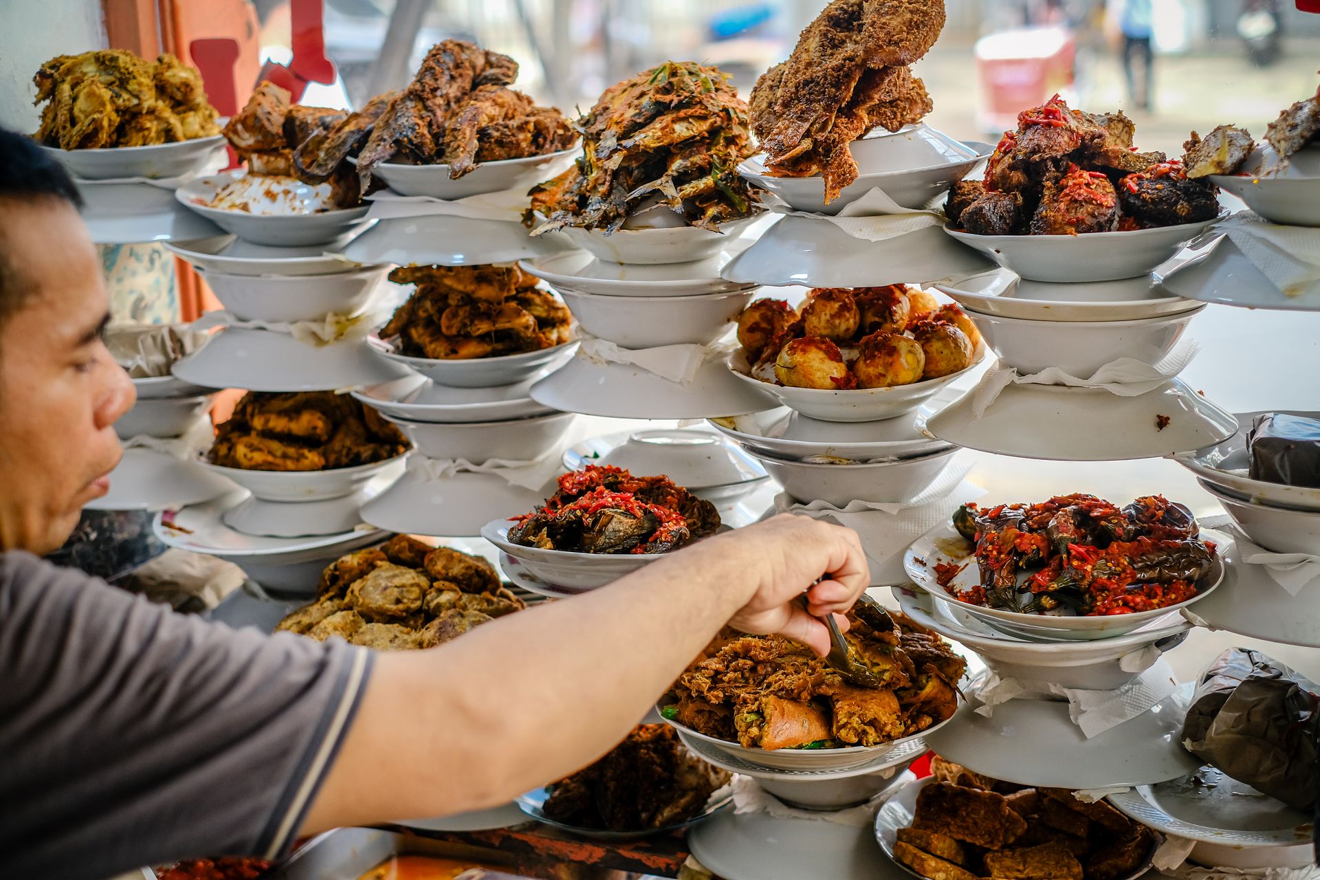 Penjual menyusun dan mengambil hidangan lauk pauk bertumpuk di etalase rumah makan Padang
