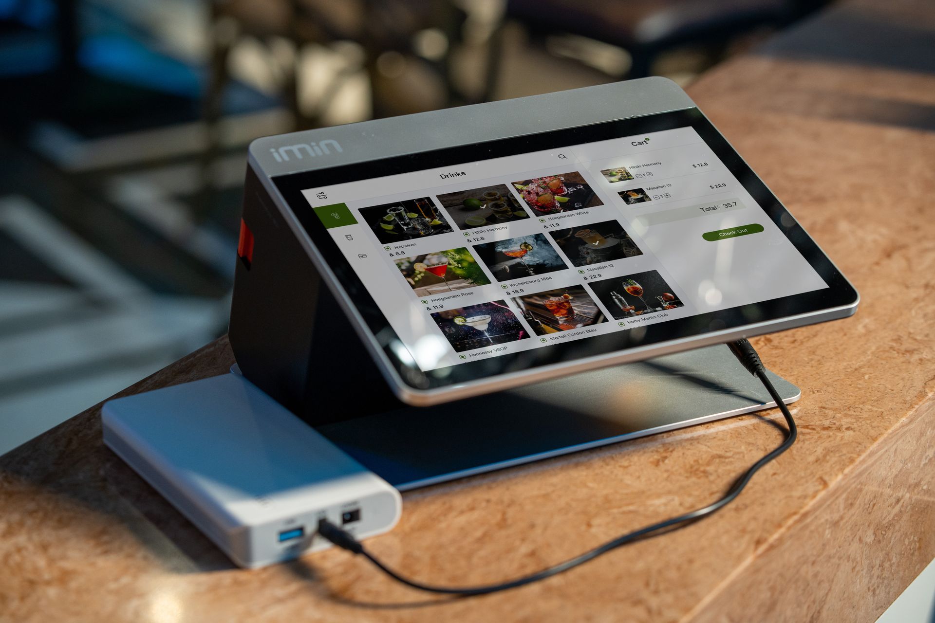 Layar perangkat POS merek iMin dengan tampilan menu digital dan power bank terhubung di meja kayu