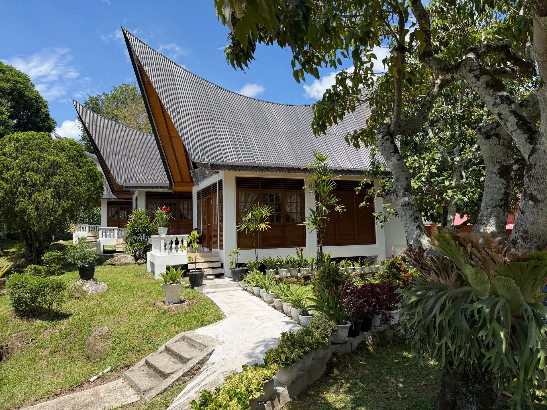 Rumah tradisional Minangkabau beratap gonjong dengan halaman taman yang asri dan pepohonan hijau