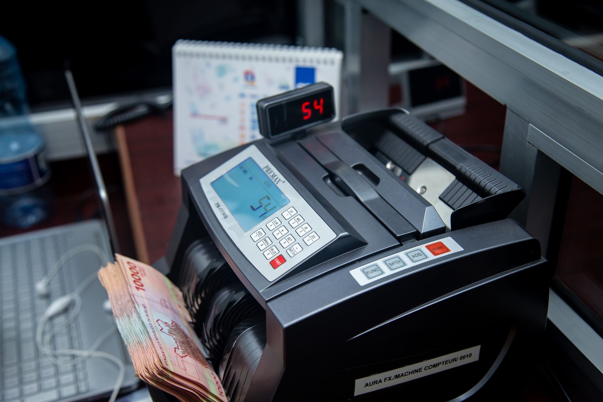 Mesin-Penghitung-Uang-Otomatis-Sedang-Menghitung-Pecahan-Rupiah Mesin penghitung uang digital dengan layar digital sedang menghitung tumpukan uang kertas pecahan rupiah di meja kerja