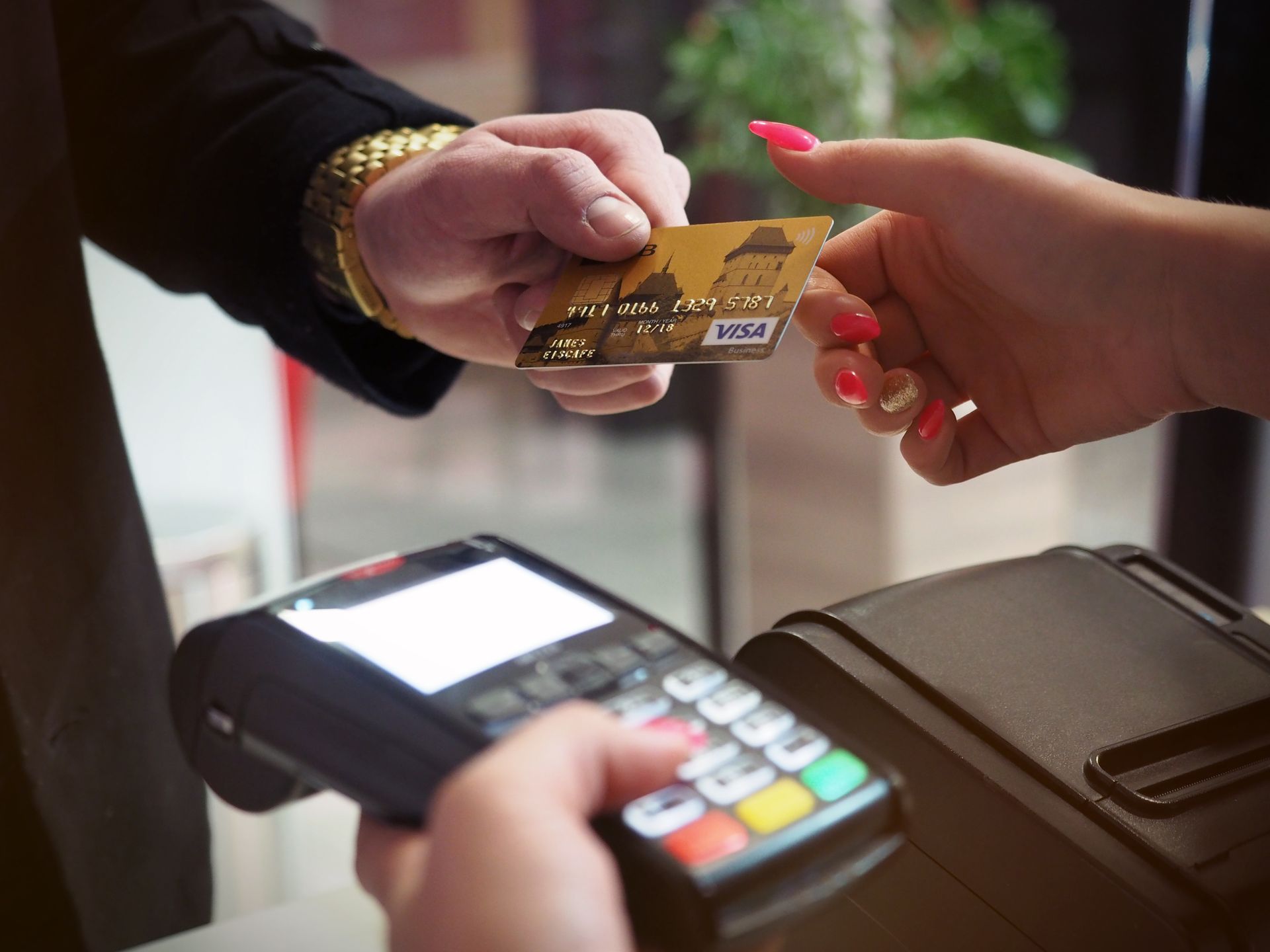 Pelanggan menyerahkan kartu kredit Visa emas kepada kasir wanita yang memegang mesin EDC di meja counter
