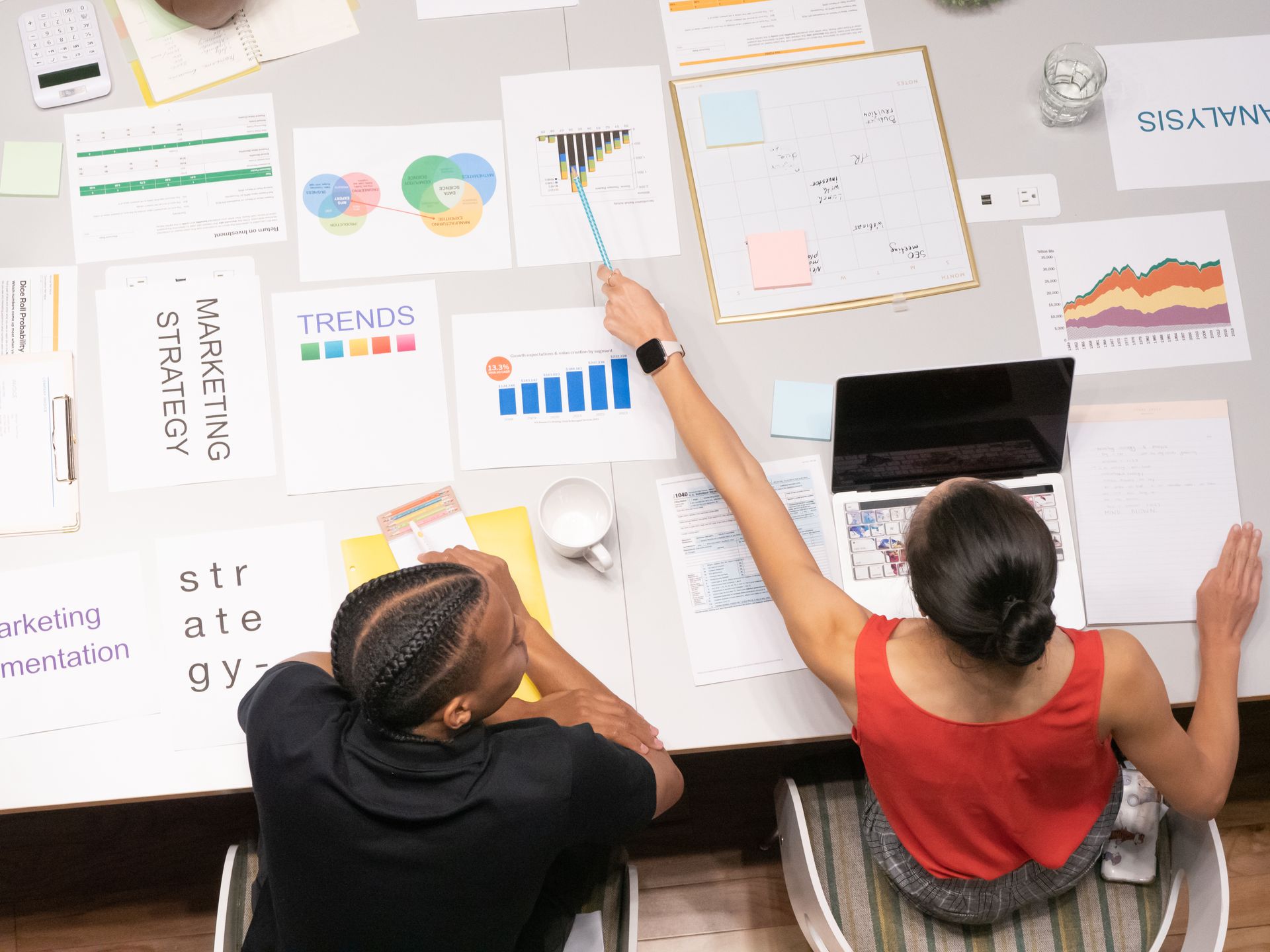 Rapat-Analisis-Data-dan-Strategi-Pemasaran-dari-Sudut-Pandang-Atas Tangkapan layar dari atas memperlihatkan dua orang sedang menganalisis dokumen grafik, tren, dan strategi pemasaran di atas meja