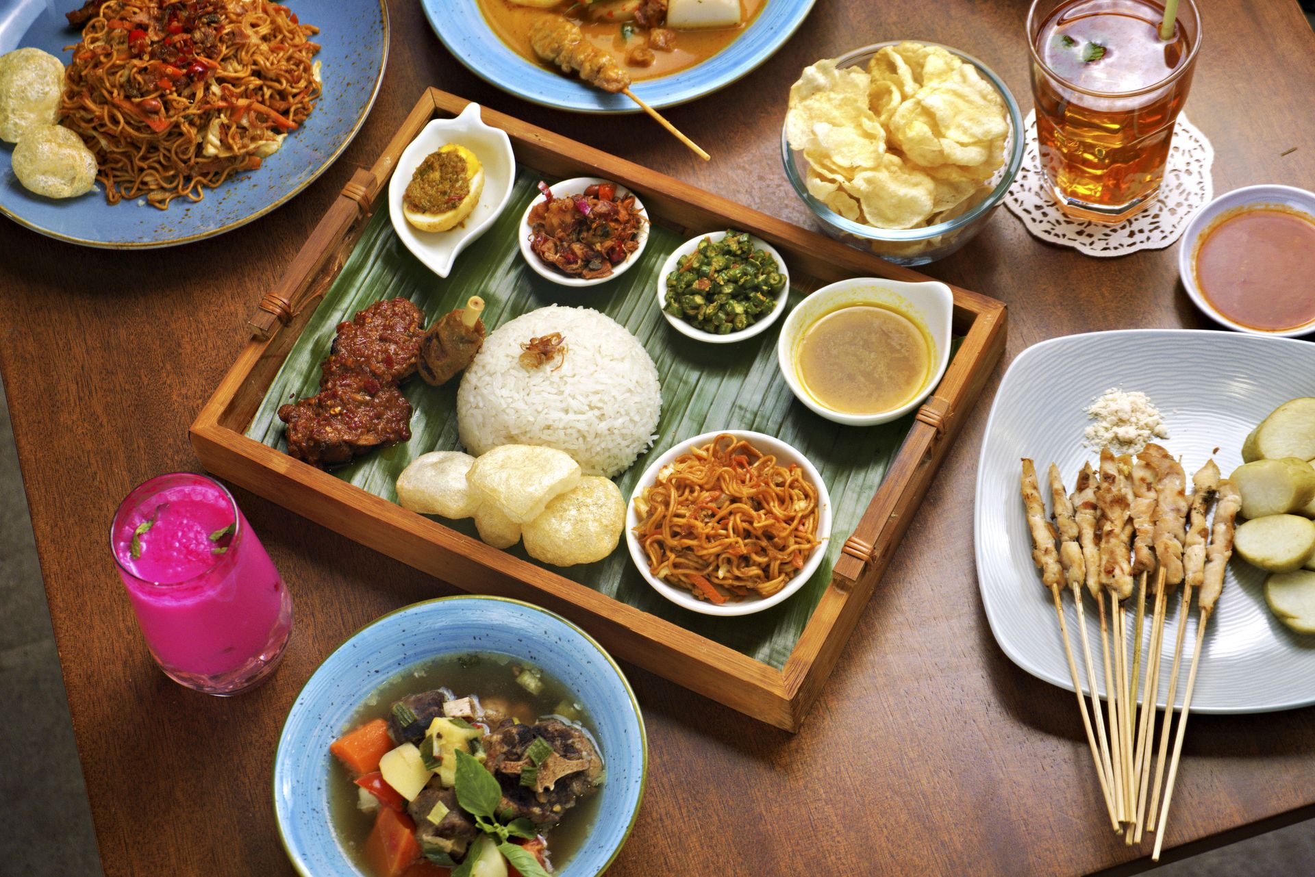 Sajian lengkap kuliner Nusantara seperti nasi campur set nampan kayu, sate, sup buntut, mie goreng, dan minuman segar di meja restoran