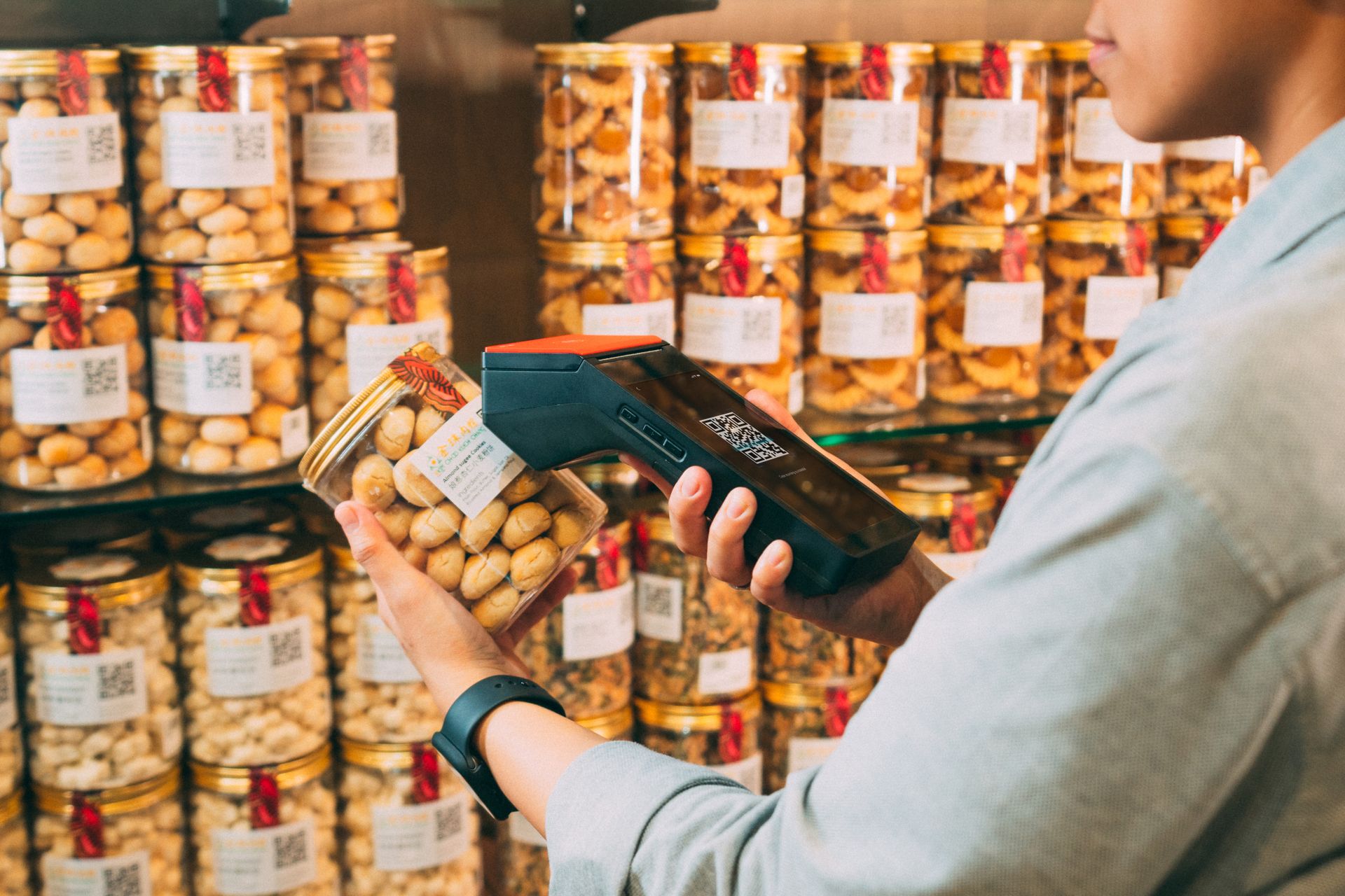 Petugas toko melakukan pemindaian kode pada kemasan toples kue kering menggunakan perangkat mesin POS genggam.