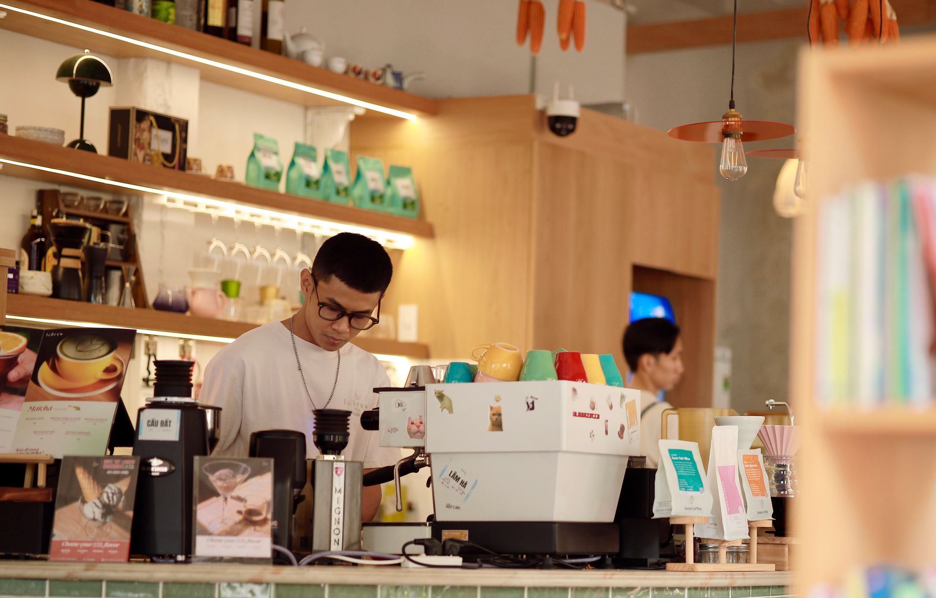 Seorang barista berkacamata meracik kopi di balik meja bar kafe modern yang estetik