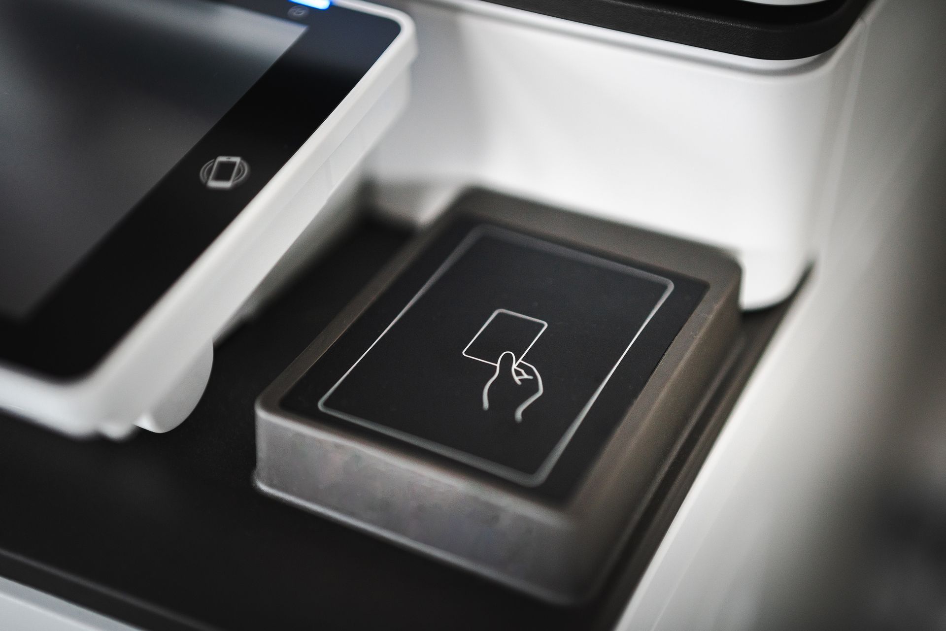 Close-up pad pembaca kartu pembayaran contactless dengan ikon tangan memegang kartu di atas permukaan mesin kasir modern