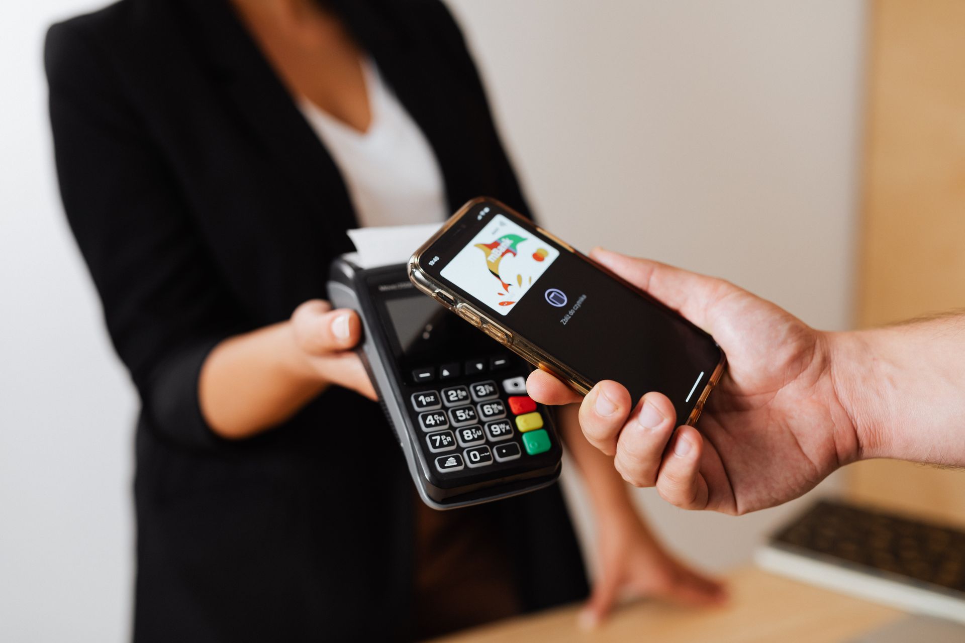 Pelanggan menempelkan smartphone ke mesin EDC terminal kasir yang dipegang staf berjas hitam untuk transaksi contactless non-tunai