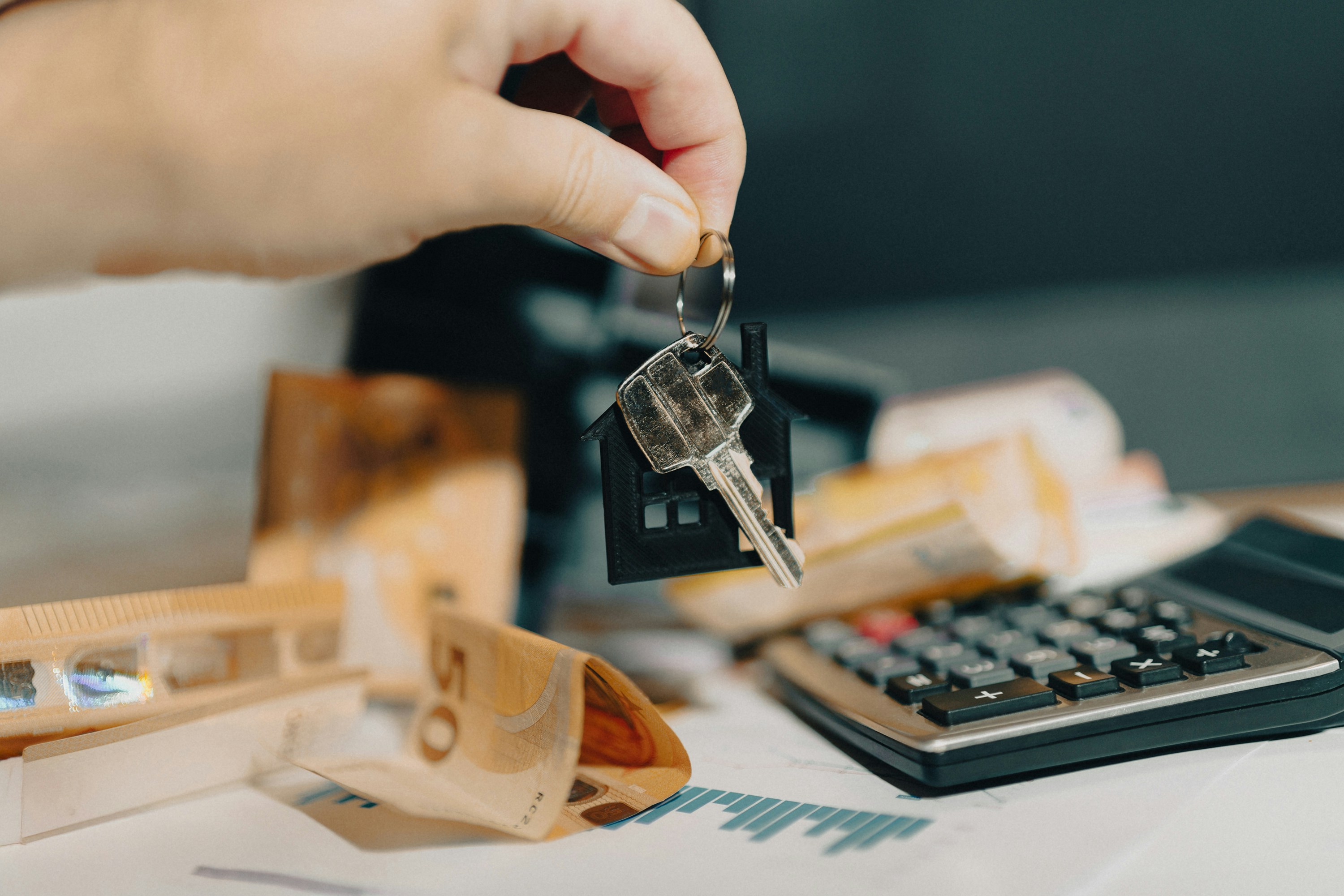 transaksi-pembayaran-bisnis-properti-dan-investasi-kasair Tangan memegang kunci rumah di atas kalkulator dan uang tunai untuk kalkulasi pembayaran sewa properti berbasis Kasair POS