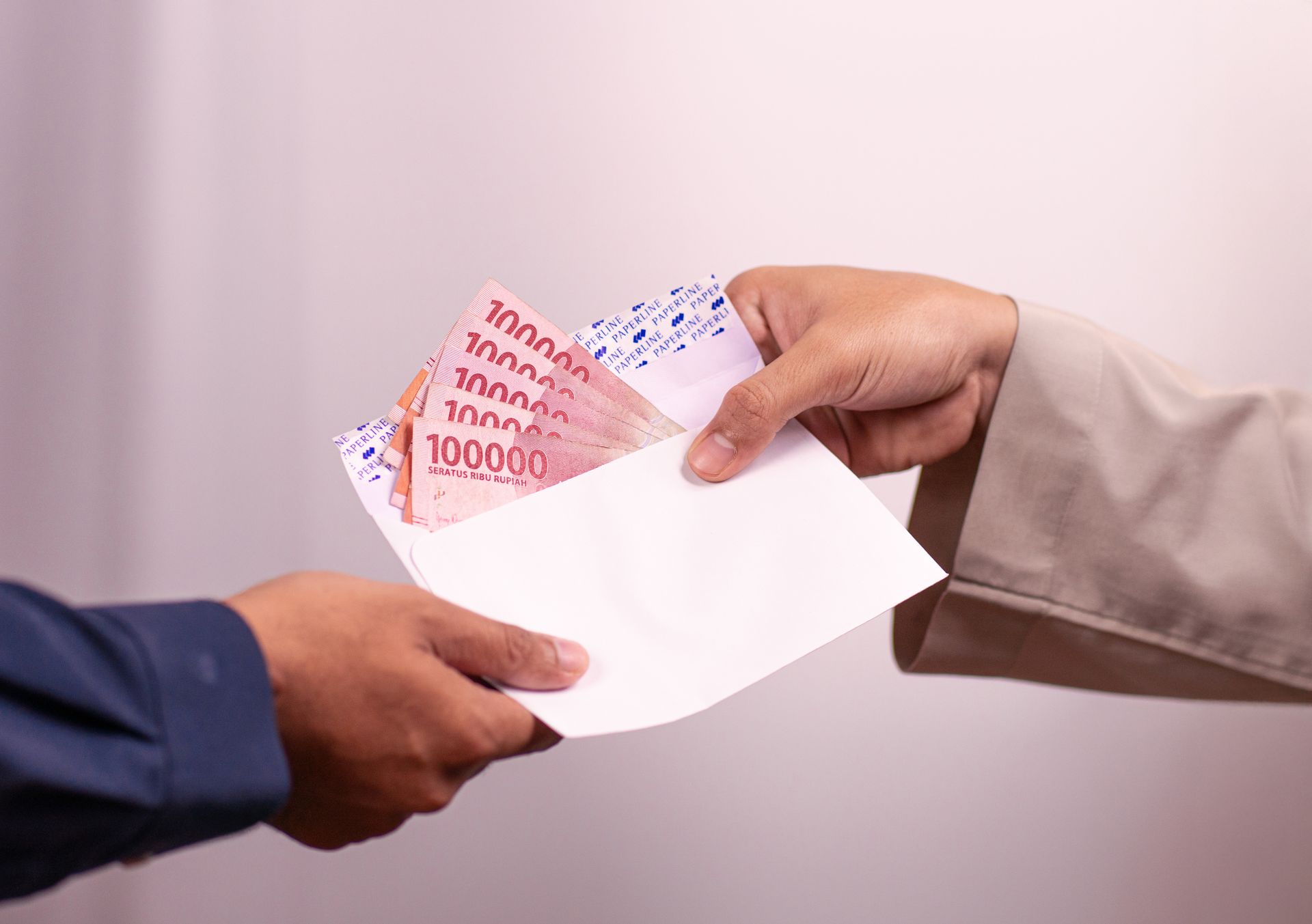 uang-pinjaman Proses serah terima amplop putih berisi lembaran uang tunai pecahan seratus ribu Rupiah antar dua orang.