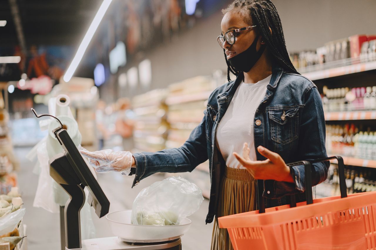 Pelanggan wanita mengoperasikan layar sentuh timbangan digital mandiri untuk menimbang belanjaan buah dan sayur di supermarket
