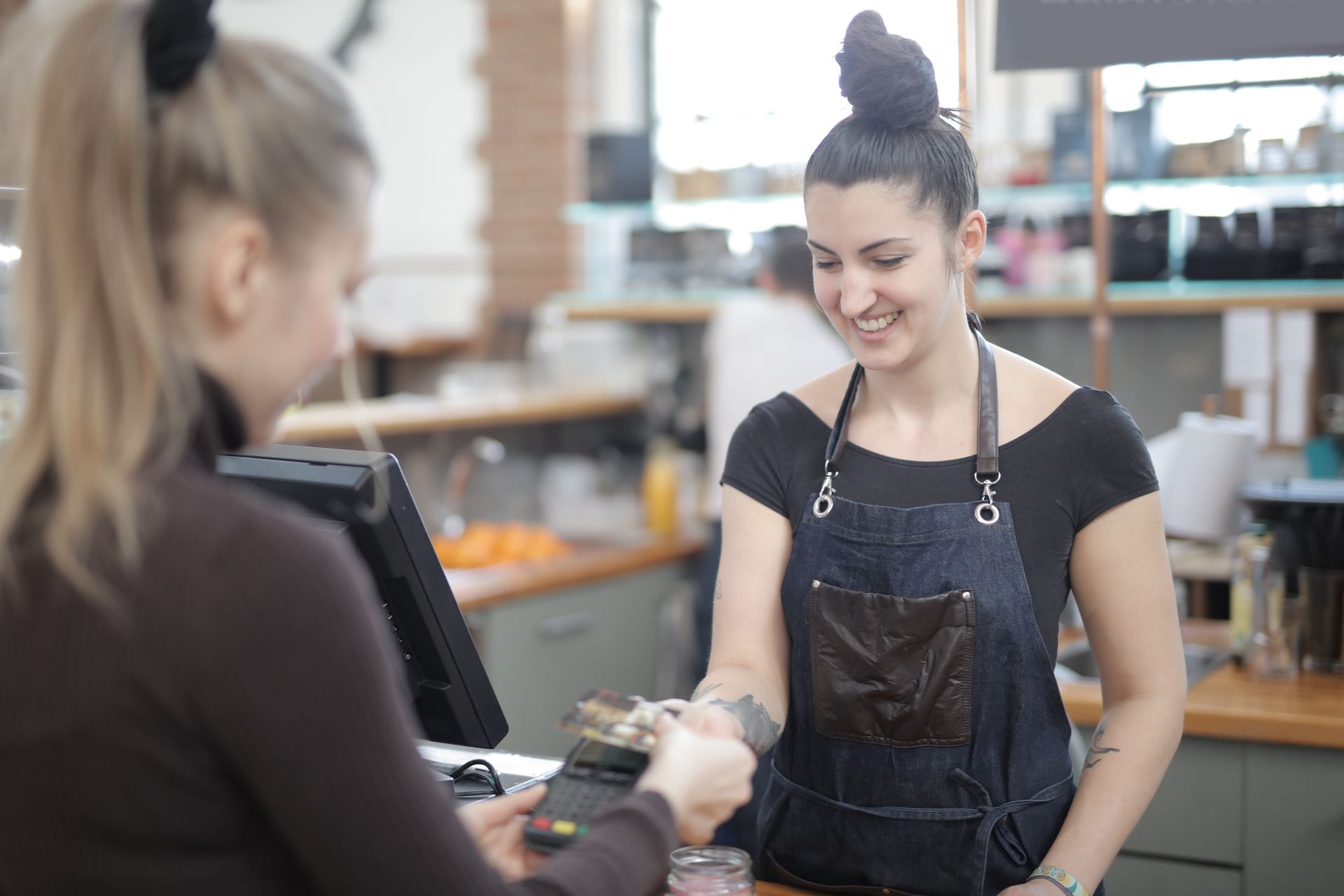 kasir cafe Kasir wanita berapron denim tersenyum saat memproses pembayaran kartu kredit pelanggan menggunakan mesin EDC.