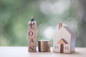 aplikasi-kasir-bank-loan-kasair Ilustrasi miniatur rumah, koin uang, dan balok kayu bertuliskan LOAN untuk pengajuan pinjaman modal usaha Kasair POS